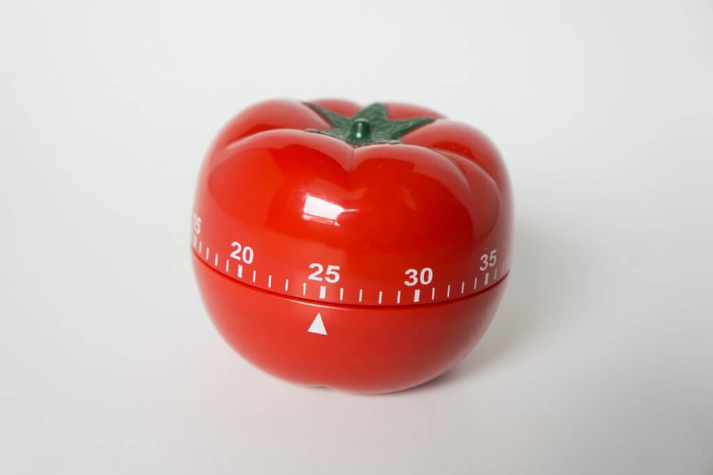 Close up view of mechanical tomato shaped kitchen clock timer for cooking & studying. Used for pomodoro technique for time and productivity management. Isolated on white background, set at 25